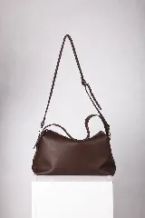 Cartera marrón de cuero suave, con diseño flexible tipo slouchy. Cuenta con cierre metálico superior, doble correa fija corta y una correa larga regulable y desmontable.