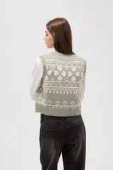 Chaleco tejido de punto con diseño jacquard de corazones y motivos geométricos en tonos verde y rosa. Presenta escote en V, cierre frontal con botones y terminaciones acanaladas en cuello, sisas y ruedo.