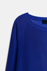 Jersey de punto liso, color azul brillante, con cuello redondo y manga larga. Presenta acabados en rib en puños, cuello y bajo, con aberturas laterales en el ruedo.