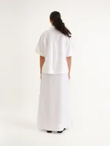Camisa de manga corta blanca, con cuello camisero, cierre frontal de botones y diseño recto.
