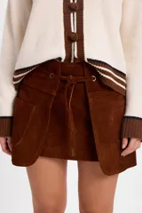 Minifalda de cuero color marrón, de silueta recta y diseño con capas frontales superpuestas. Cuenta con un lazo ajustable en la cintura que pasa por ojalillos metálicos.