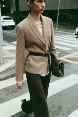Blazer de corte clásico con cuello solapa y manga larga, confeccionado en tejido con patrón de espiga en tonos tierra y líneas verticales en color salmón. Cuenta con bolsillos delanteros y cierre frontal con botones ocultos.