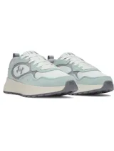 Championes Under Armour modelo Mirage Sport, con diseño de inspiración retro. Presentan una combinación de malla transpirable con superposiciones de gamuza y cuero en tonos verde agua y gris. Incluyen entresuela de EVA acolchada y suela de goma resistente, con el logotipo de la marca en detalle tipo joya en el lateral.