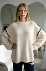 Sweater de punto gris con textura suave, diseño oversize, cuello redondo y detalles de costuras expuestas en color blanco en mangas y ruedo.