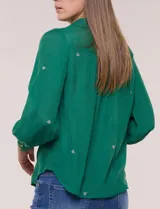 Camisa de estilo boho, color verde, con cuello camisero, escote en V y botonadura frontal con botones perlados. Cuenta con una pechera con bordados geométricos y florales a contraste, mangas largas abullonadas con puños abotonados y delicados bordados dispersos.