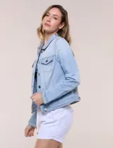 Camperita de denim clásico con lavado claro, cuello camisero, cartera frontal con botones metálicos y bolsillos superiores con solapa. Presenta mangas largas con puños abotonados y costuras estructuradas.