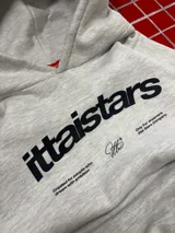 Hoodie gris jaspeado con capucha, bolsillo frontal tipo canguro y estampado gráfico en el pecho con la marca ittaistars.