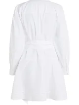 Vestido camisero corto color blanco, confeccionado en algodón orgánico. Presenta cuello en V, cierre frontal con botones, mangas largas abullonadas, cinturón de lazo ajustable en la cintura, bolsillos laterales y detalle de encaje calado en forma de escalera.