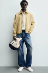 Cazadora regular fit de color beige, confeccionada en mezcla de algodón y lyocell. Cuenta con cuello camisero, cierre frontal de cremallera, bolsillos de plastrón en la cadera, mangas largas con puños elásticos y bajo con ajuste elástico.