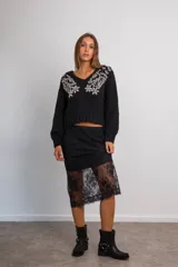 Buzo de punto negro con escote en V, manga larga y diseño holgado. Presenta detalles bordados con canutillos y pedrería en forma de flores y ramas sobre los hombros y el pecho.