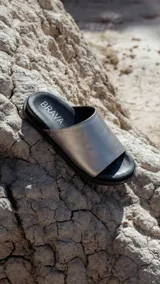 Sandalias planas negras tipo slide, con capellada ancha de pelo corto. Tienen suela de caucho expandido y base plana de 3 cm de altura.