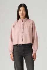 Camisa color rosa pálido, de corte cropped, con cuello camisero, cierre frontal con botones, mangas largas abullonadas con puños elásticos, dos bolsillos de parche en el pecho y canesú en la espalda.