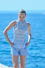 Blusa celeste de encaje sin mangas, con cuello alto vuelto y acabado ondulado en el ruedo.