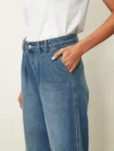 Jean de corte wide leg en color azul medio, con diseño de tiro alto y pinzas en la cintura. Presenta un estilo holgado y relajado con costuras reforzadas en el ruedo.