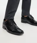 Zapato de vestir negro, confeccionado en cuero sintético, con puntera cuadrada, cierre con cordones y suela de goma.