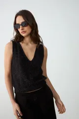 Musculosa de punto color negro con sutil brillo plateado, escote en V pronunciado y ribetes acanalados en el ruedo.
