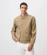 Sobrecamisa de sarga de algodón en color beige, de corte amplio y estructurado, con cuello camisero, mangas largas, cierre frontal de botones ocultos y grandes bolsillos frontales con solapa.