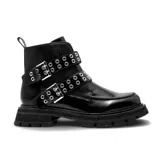 Bota corta de estilo militar en color negro, confeccionada en cuero sintético con acabado brillante. Presenta doble tira con hebillas metálicas y ojales decorativos, suela track dentada y textura acanalada en la parte superior de la caña.