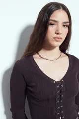 Top de tejido acanalado color negro, con escote en V y cierre frontal mediante cordones ajustables con ojales metálicos. Presenta mangas largas y un corte entallado al cuerpo.