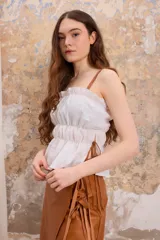 Top blanco con frunces, tirantes finos de cuero y detalle de lazos en los laterales.