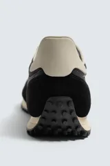 Zapatilla de estilo retro con cordones, confeccionada en una combinación de materiales textiles y piezas de cuero con acabado serraje. Presenta una suela dentada en contraste de color.