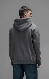 Hoodie oversize color gris oscuro, confeccionado en frisa premium con textura gamuzada. Presenta capucha ajustable con cordones personalizados, bolsillo frontal tipo canguro y puños con abertura para el pulgar.