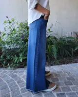 Pantalón de jean color beige, de corte recto y tiro alto, con ruedo deshilachado y cierre frontal con botón y cremallera.