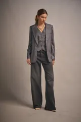 Blazer gris con rayas verticales finas, de calce amplio, con cruce recto y acceso por medio de un botón. Tiene bolsillos en el delantero y abertura en el centro de la espalda.