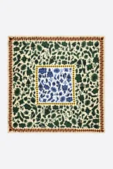 Pañuelo cuadrado confeccionado en poliéster con estampado Ikatmix. Presenta un diseño ornamental complejo con motivos florales y vegetales en tonos verdes y azules sobre un fondo crema, enmarcado por bordes decorativos en tonos amarillos y marrones.