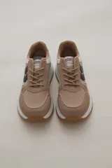Zapatilla deportiva de diseño urbano, combinando paneles de tela blanca y gamuza sintética en tono gris claro. Cuenta con cordones grises, suela de plataforma con entresuela blanca y base dentada en color caramelo.