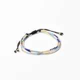 Pulsera elástica de tres hilos con cuentas de vidrio en tonos azul, blanco y dorado, con cierre corredizo de cordón negro.