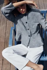 Chaqueta de cuero gamuzado color gris, con cuello redondo, manga larga, cierre frontal con botones oscuros y bajo con detalle peplum.