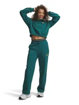 Pantalón de corte holgado en tejido French Terry color verde petróleo. Presenta cintura elástica con cordón ajustable, bolsillos laterales y detalle de pliegue frontal. Incluye un pequeño parche bordado con diseño de estrella y letras en la parte superior del muslo.