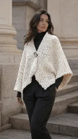 Poncho corto de lana natural en color crudo, con textura tejida marcada, corte amplio y envolvente, y cierre frontal con un botón central.