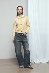 Cardigan de punto color amarillo claro, con cuello camisero, mangas largas y cierre frontal de botones multicolor. Presenta costuras con pespuntes en contraste de color azul en el cuello, los puños y el ruedo.