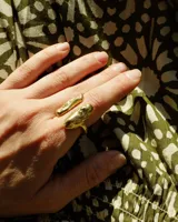 Anillo de diseño orgánico y macizo con forma irregular, elaborado en metal con acabado brillante. Presenta una estructura abierta que permite su ajuste.