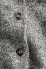 Cárdigan corto de punto suave, color gris jaspeado, con cuello camisero, abotonadura frontal y remates acanalados en puños y bajo.