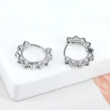 Par de aros pequeños plateados con forma de sol y pequeños brillantes incrustados.