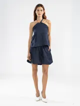 Top halter azul marino confeccionado en lino italiano con hilo metalizado, que aporta un sutil efecto de brillo y una textura natural. El escote halter se ajusta mediante un cordón al cuello, donde se ubica la insignia del tigre Polonio, fácilmente removible al deslizar el cordón.