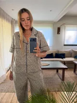 Pijama de dos piezas, compuesto por una camisa de manga corta con cuello y ribetes en color azul marino, y pantalón largo. El conjunto presenta un estampado floral pequeño en tonos arena y marrón.