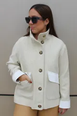Campera de paño color beige con cuello alto, cierre frontal de botones y bolsillos frontales con solapa blanca. Presenta puños vueltos en color blanco.