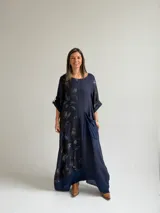 Vestido largo azul oscuro con diseño asimétrico que combina un lado liso con un lado estampado de hojas, manga corta y bolsillo frontal aplicado.