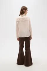 Camisa de poliéster color crema con estampado de pequeños puntos negros, cuello clásico, cierre frontal con botones y mangas largas con puños abotonados.