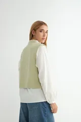Chaleco tejido de punto color verde salvia, con cuello redondo y diseño sin mangas. Presenta detalles de pequeños apliques brillantes distribuidos por toda la prenda.