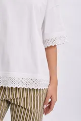 Remera manga corta de color blanco con detalles de encaje en el borde de las mangas y el ruedo, de corte holgado y diseño casual.