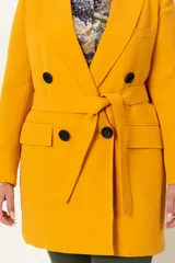 Chaqueta cruzada color mostaza con lazo y botones negros. Tiene bolsillos con tapa y detalle de cuatro botones en las mangas.