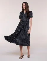 Vestido midi negro con estampado de lunares blancos, de la marca Sharagano. Presenta cuello con solapa, escote en V, cierre frontal con botones y mangas cortas. Tiene un corte en la cintura con lazo ajustable y falda plisada.
