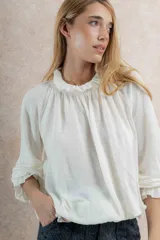 Blusa color crema de tela tejida 100% lana, con cuello fruncido y mangas largas con puños elásticos.