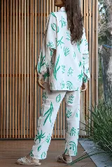 Conjunto de dos piezas compuesto por camisa de corte oversize con mangas largas y pantalón de corte recto, ambos confeccionados en tela color crudo con estampado botánico en color verde.