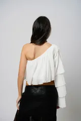 Blusa blanca con un hombro descubierto, manga larga con volados y textura arrugada.